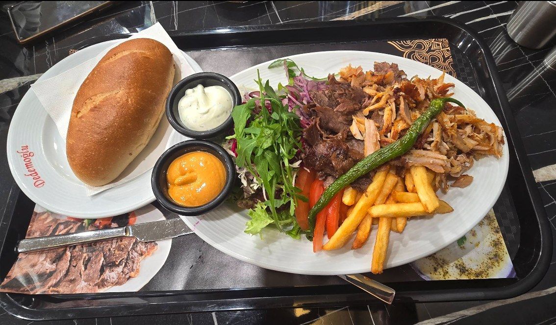 Dönerteller mit Pommes, Salat, Brot und zwei Soßen auf dem Tablett